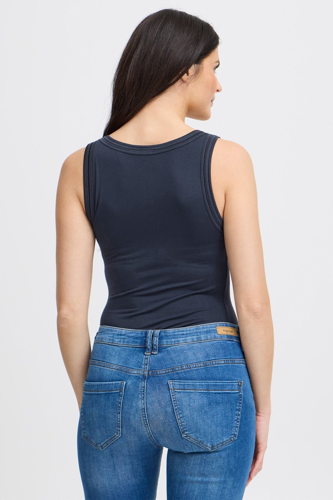 Woman wearing a navy tank top and blue jeans on a white background