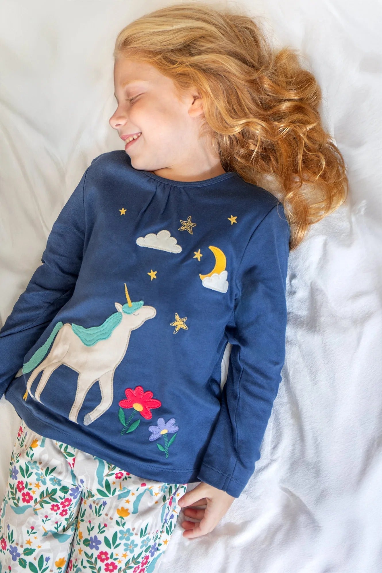 Child wearing a blue shirt with unicorn and floral designs, lying on a white surface.