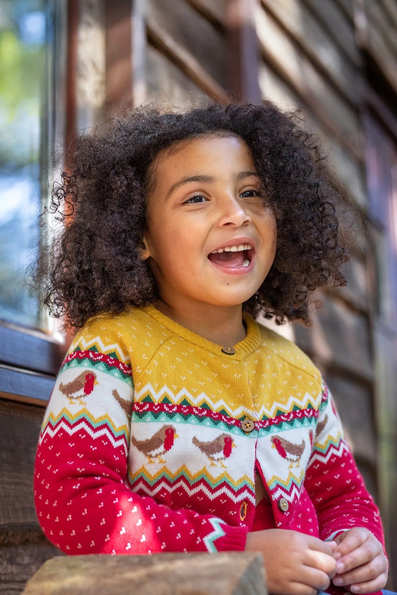 Child wearing a colorful sweater with a pattern of birds and zigzag designs, standing outdoors.