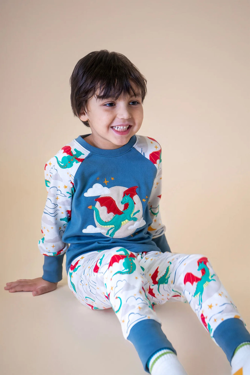 Child wearing colorful dinosaur-themed pajamas against a beige background