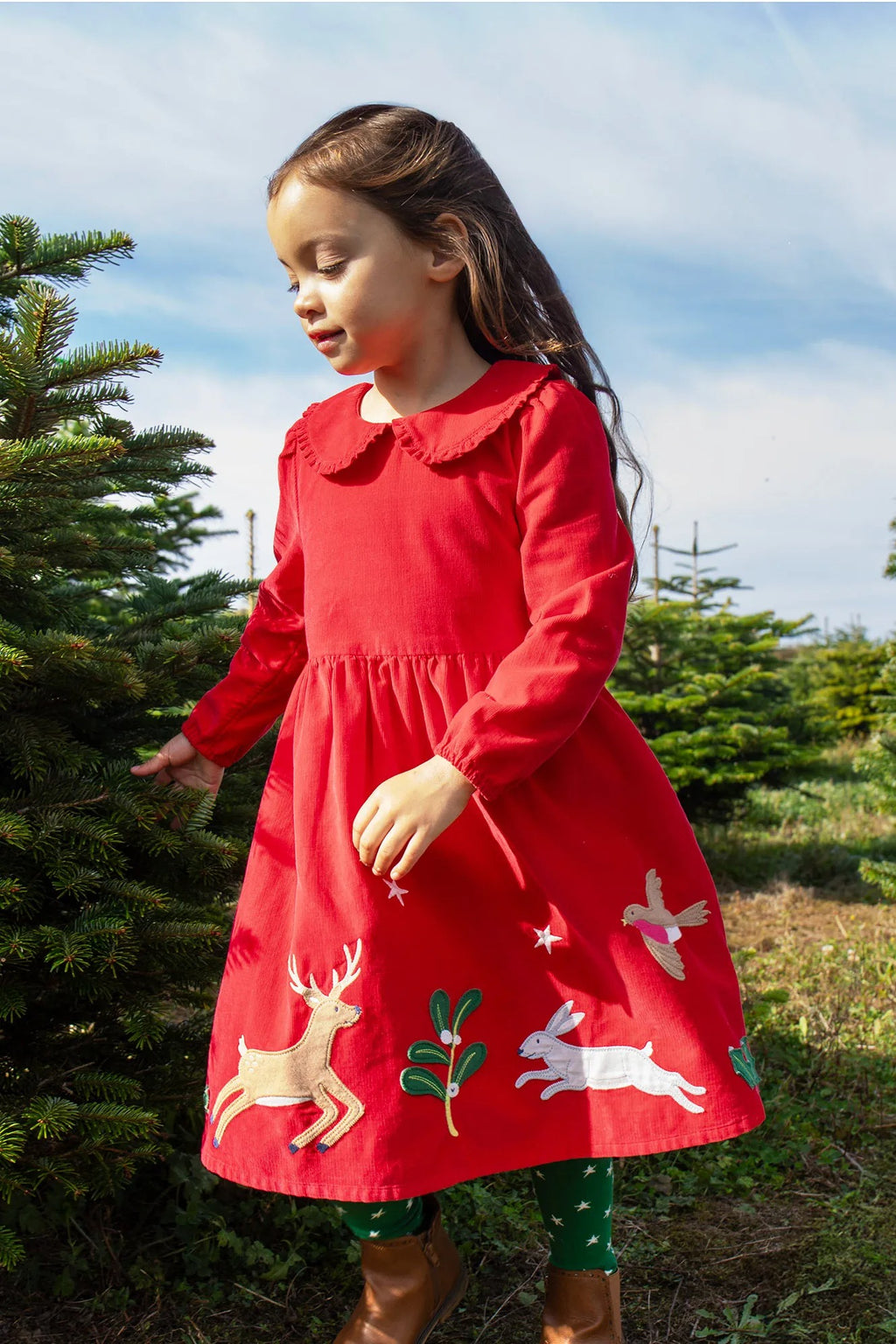 Young girl in a red dress with animal appliqués standing next to a Christmas tree.