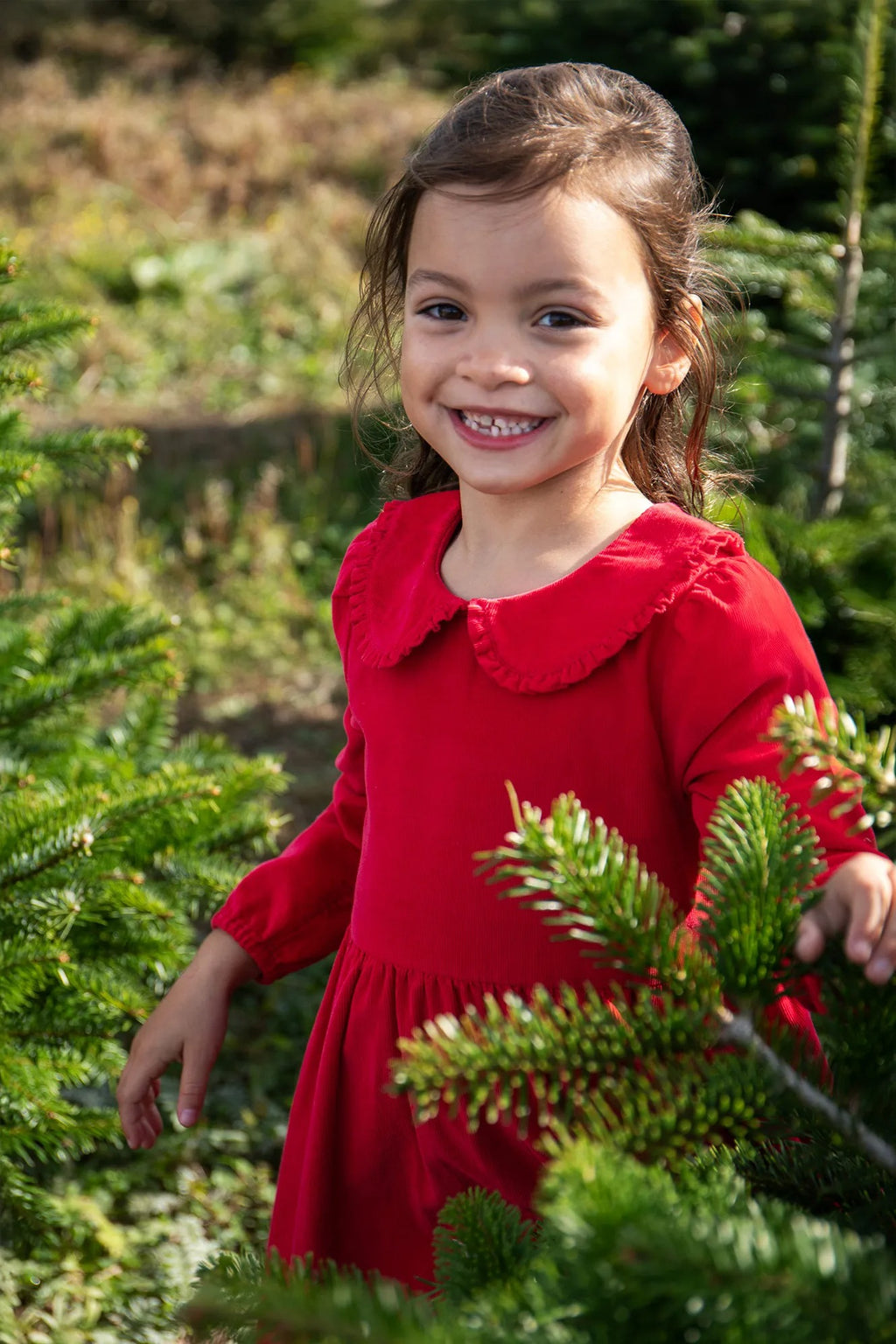 Young girl in a red dress standing among Christmas trees