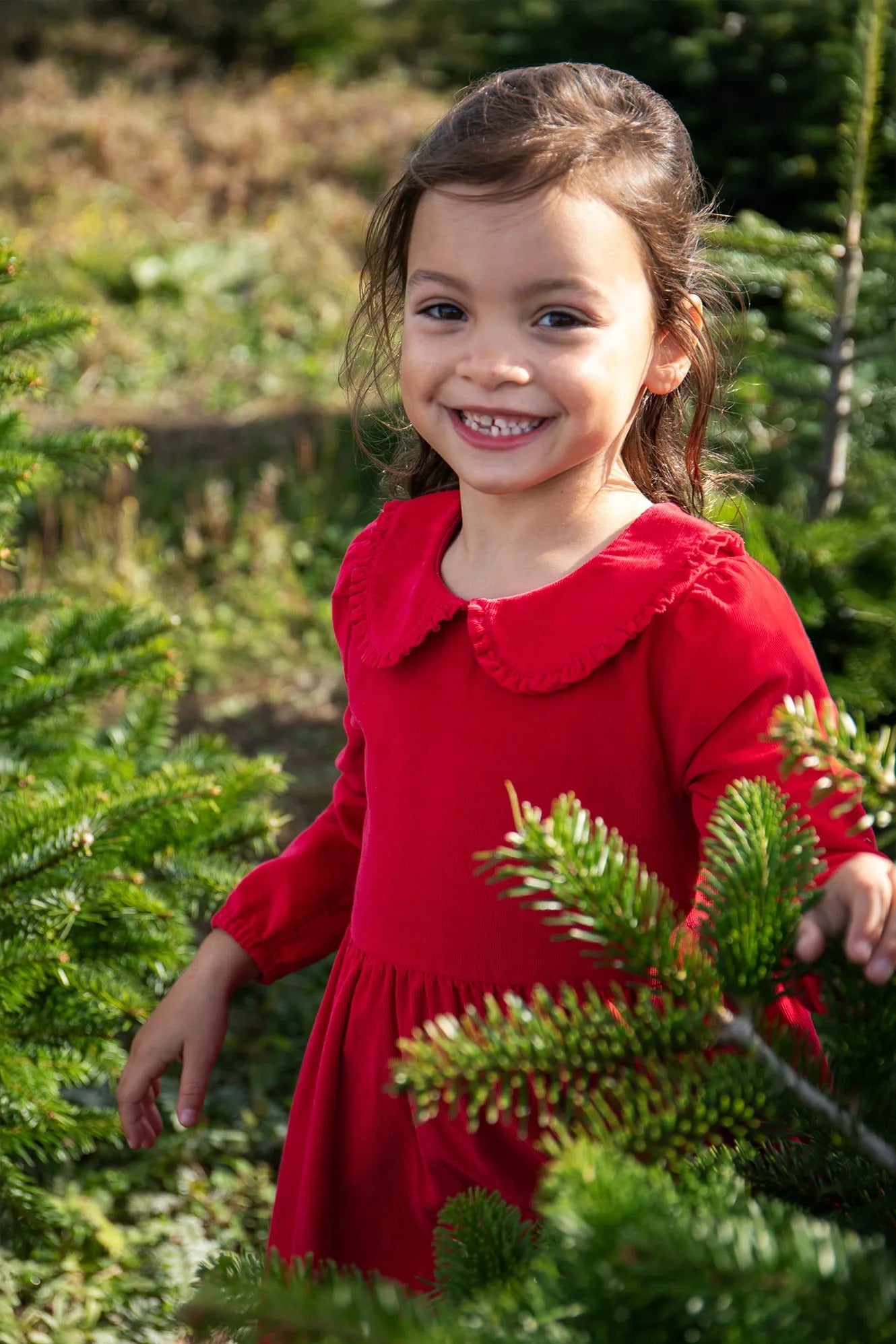Young girl in a red dress standing among Christmas trees