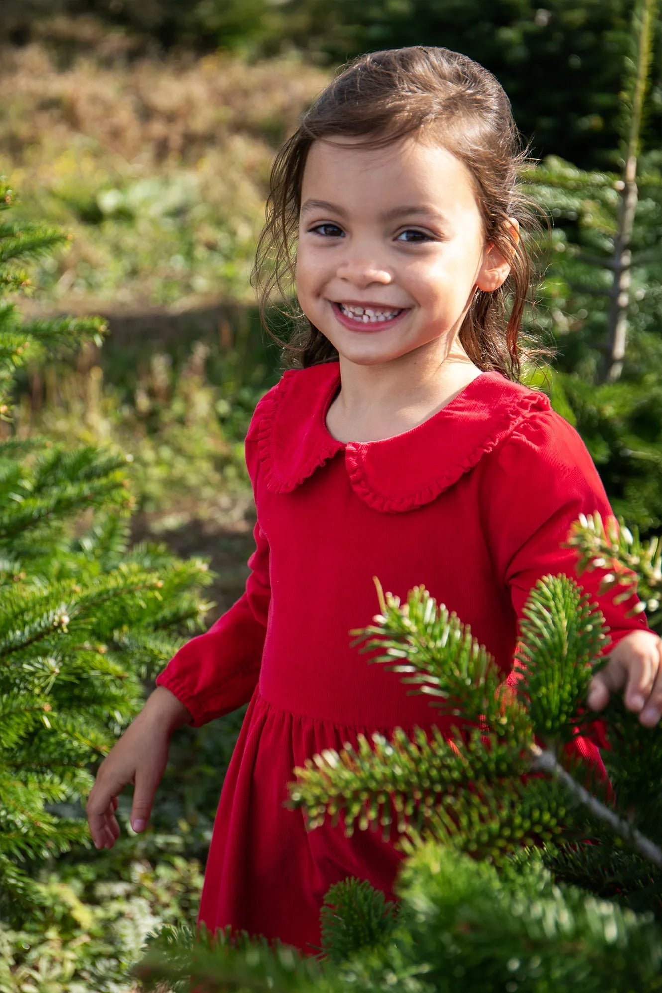 Young girl in a red dress standing among Christmas trees