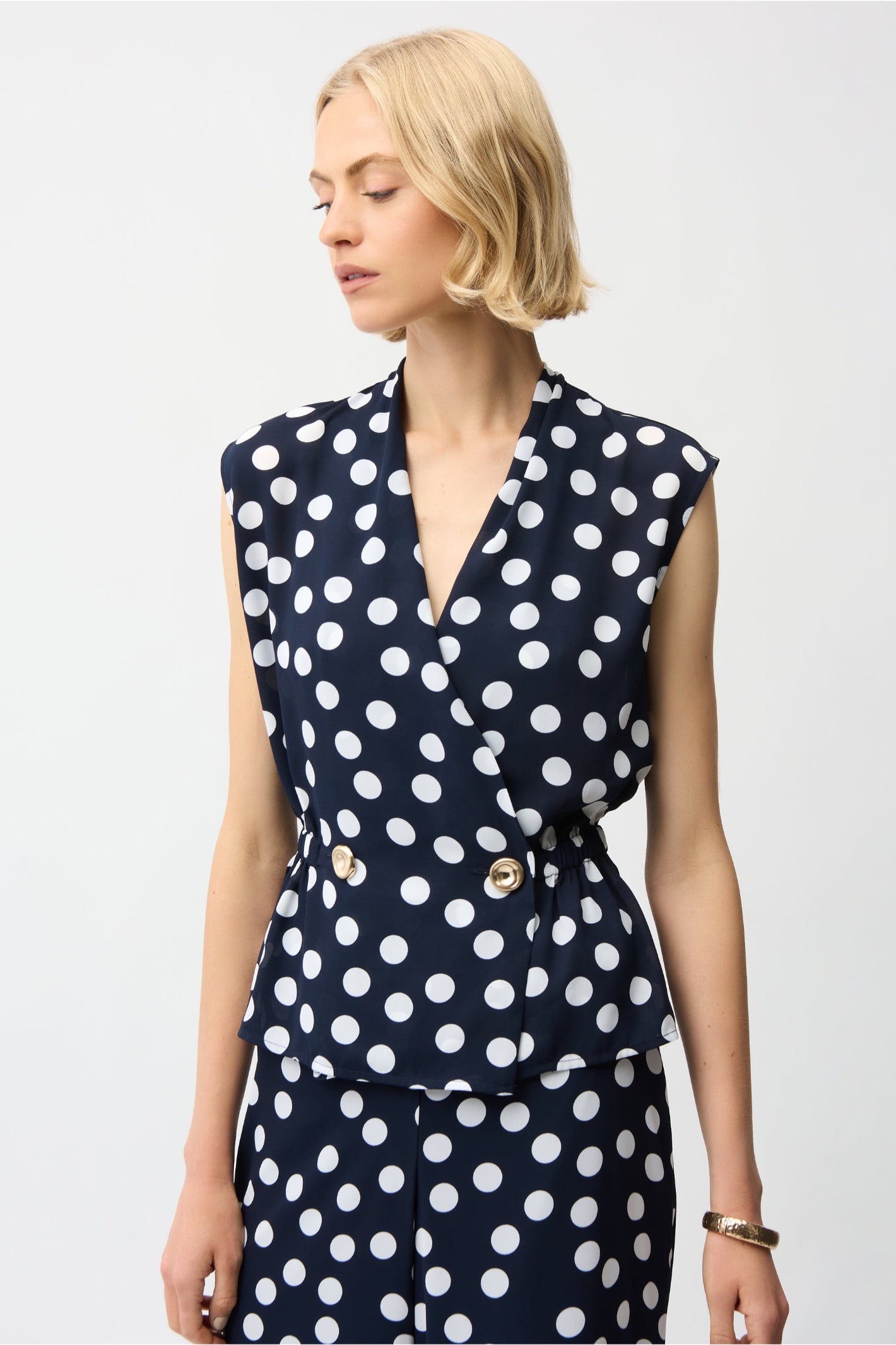 Model wearing Joseph Ribkoff 261250 Georgette Dot Print Wrap Peplum Top With Gold Buttons in navy with white dots by Joseph Ribkoff, shop Joseph Ribkoff at Dotique.