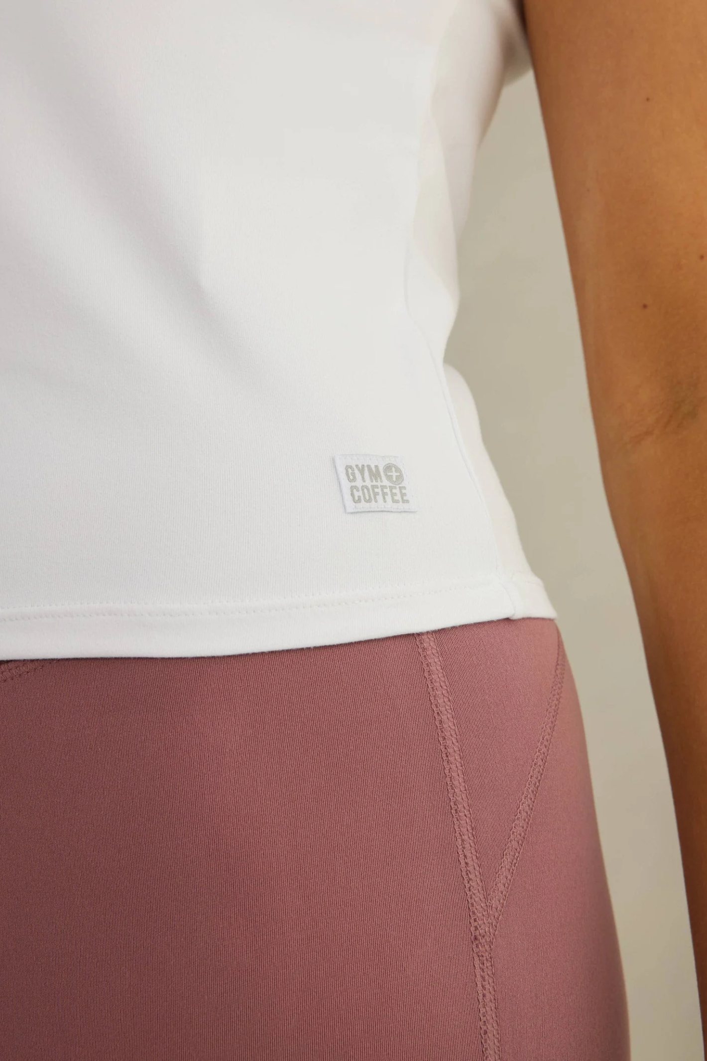 Close-up of the Gym+Coffee Daily Urban Tee in Ultra White worn with mauve leggings, shop Gym+Coffee at Dotique.