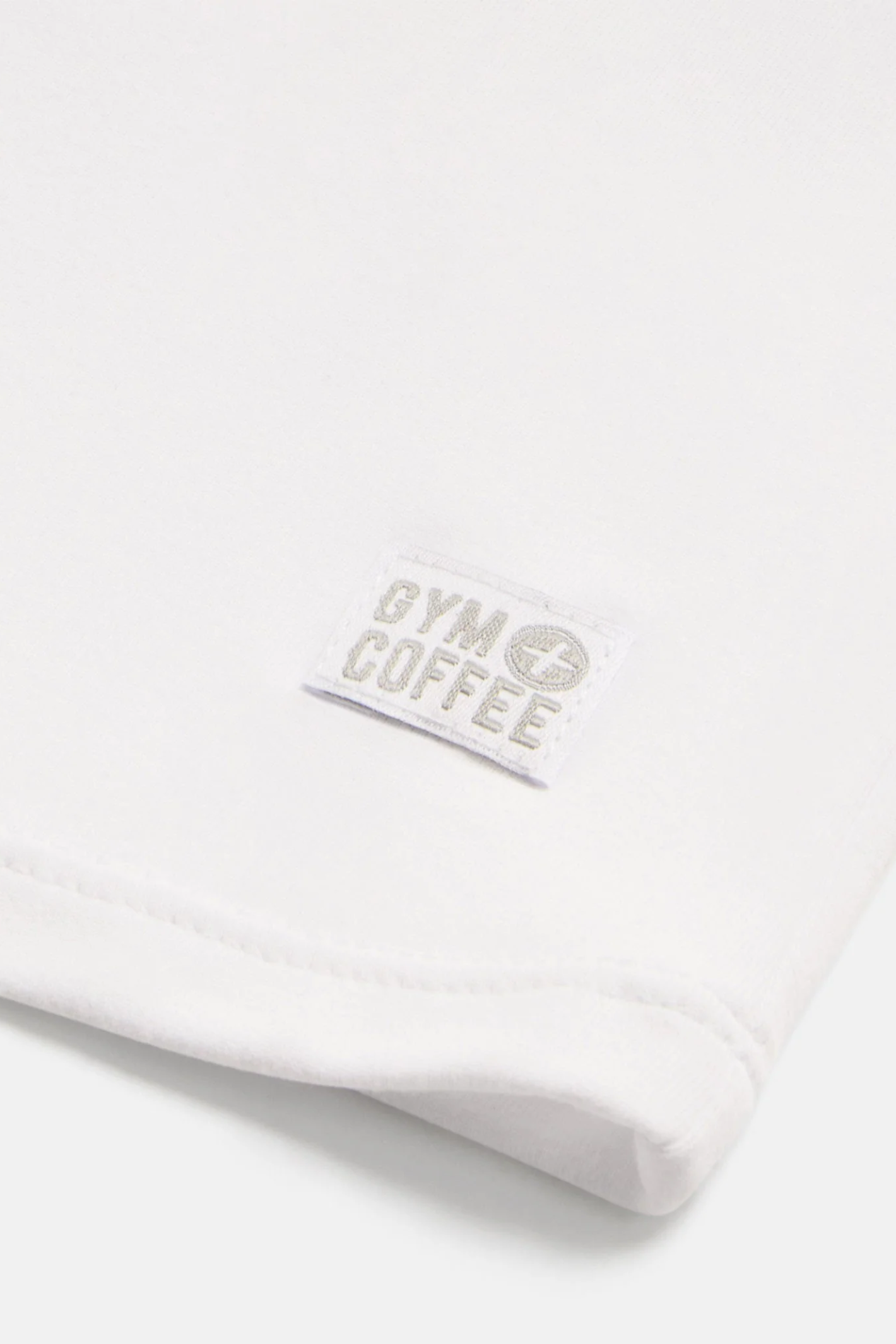 Close-up of the Gym+Coffee Daily Urban Tee in Ultra White showing the Gym+Coffee logo, shop the vendor at Dotique.