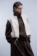 Shop the Haako H2010 sleeveless faux leather jacket in ivory. A structured vest with collar, drawstring hem and open front. A statement layering piece at Dotique.