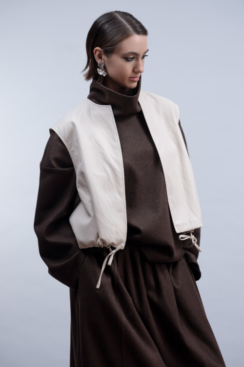 Shop the Haako H2010 sleeveless faux leather jacket in ivory. A structured vest with collar, drawstring hem and open front. A statement layering piece at Dotique.