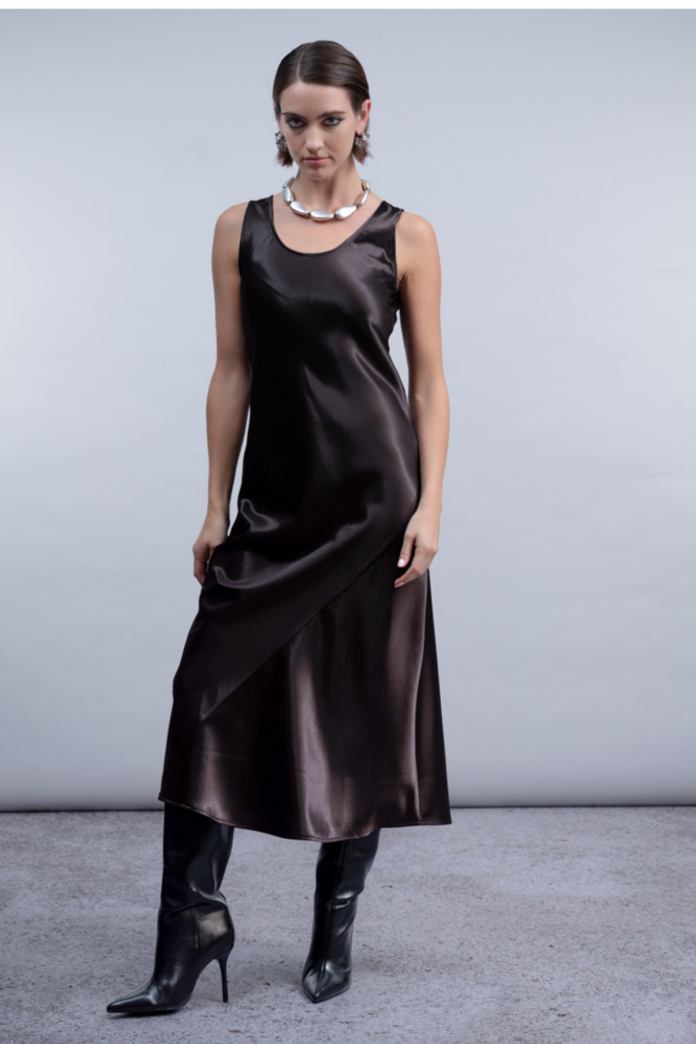 Shop the Haako H2059 brown satin slip dress with scoop neck and asymmetric hem detail. A sleek, elevated midi dress at Dotique.