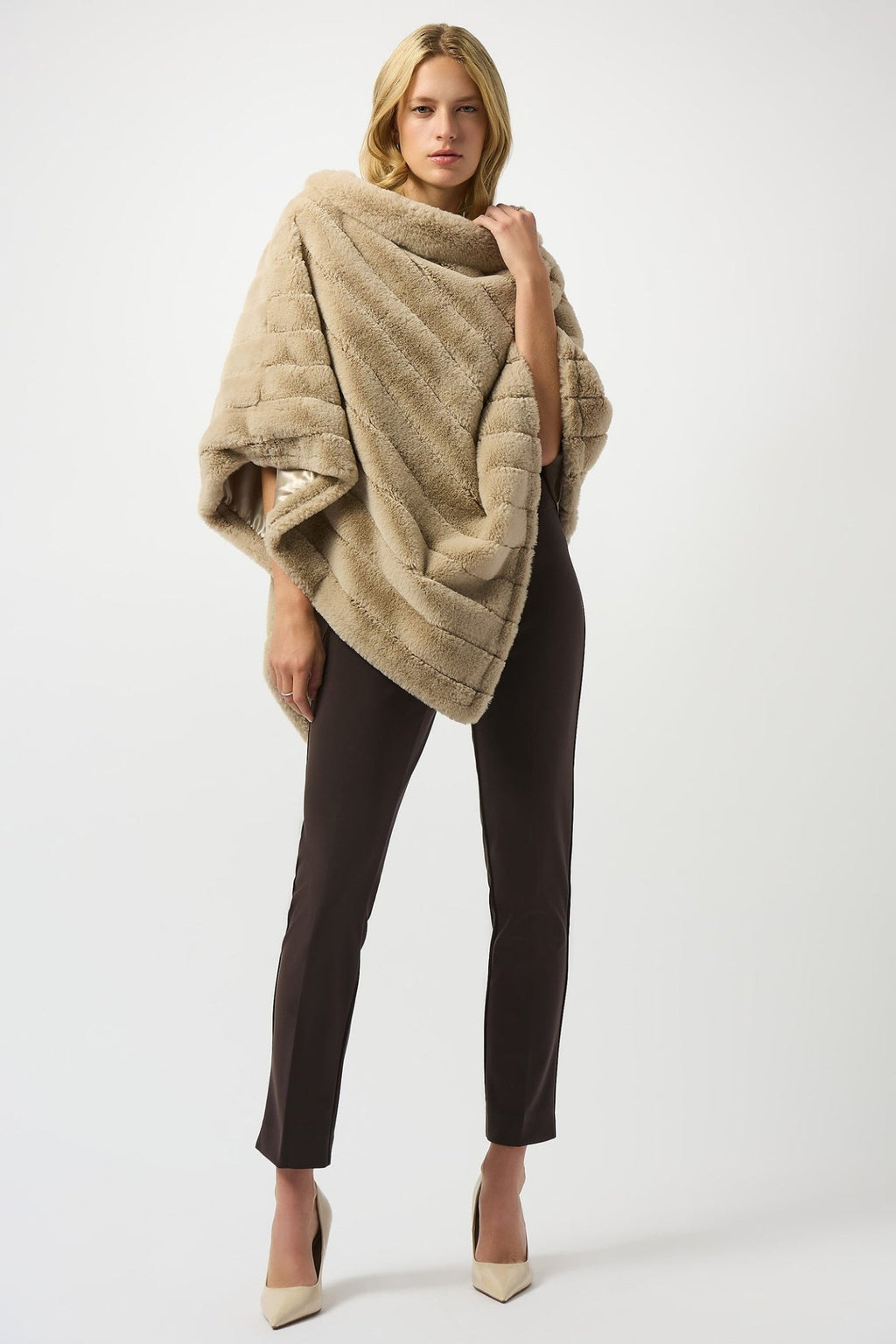 Woman wearing a beige fur poncho over a black outfit on a white background