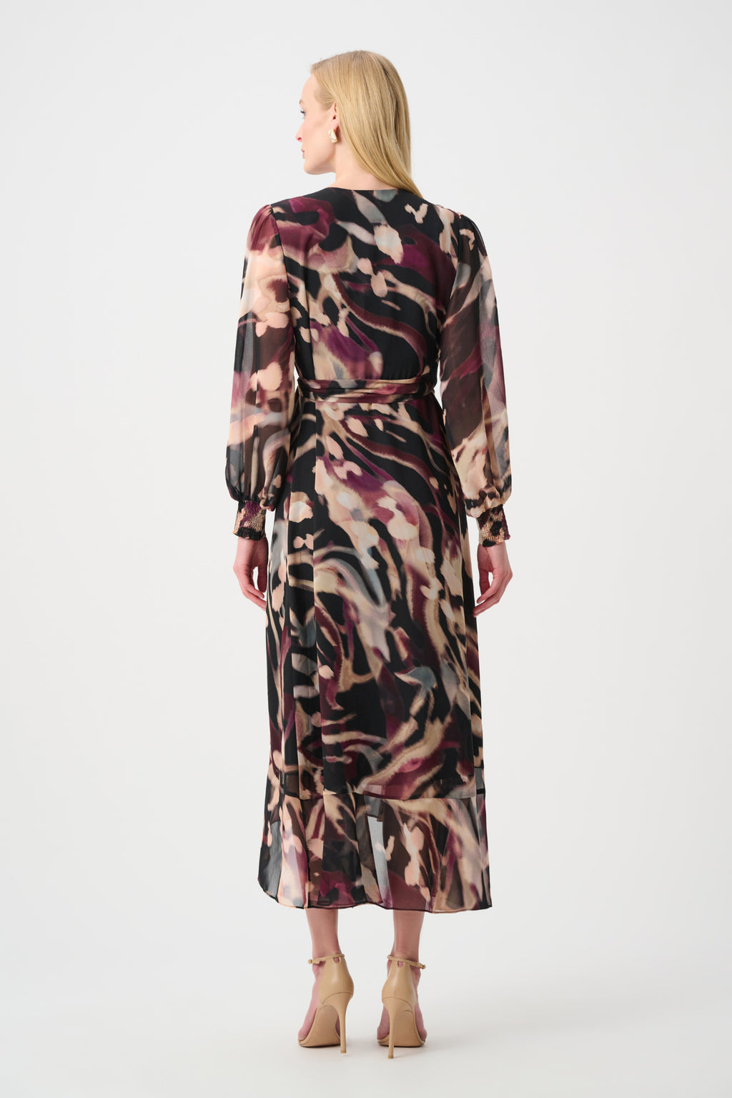 Woman wearing a long abstract print dress with long sleeves and ankle strap heels viewed from behind