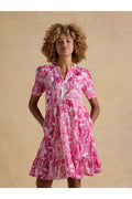 Model wearing Joules H63479 Ariella Pink Toile Tiered Dress with short sleeves and V-neck, featuring a pink toile pattern by Joules. Shop Joules at Dotique.