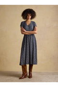 Model wearing Joules H69513 Nia Navy Jersey Dress with short sleeves and geometric pattern, styled with brown boots. Shop Joules at Dotique.
