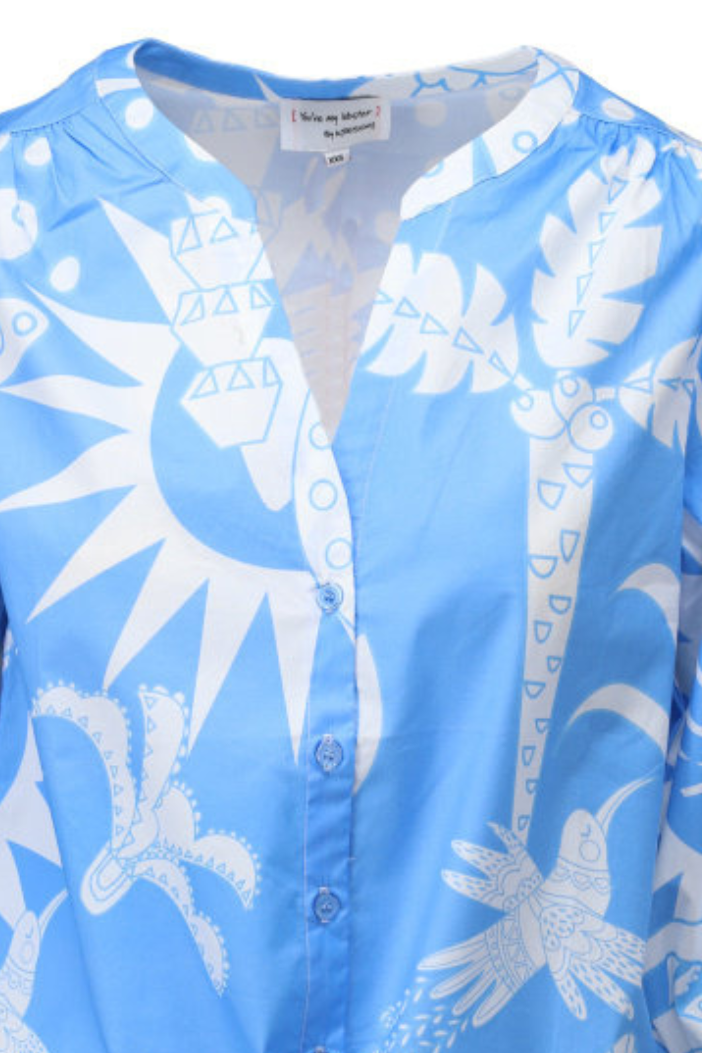 Close-up of blue blouse with abstract white sun and bird motifs, button-front, and relaxed collar design