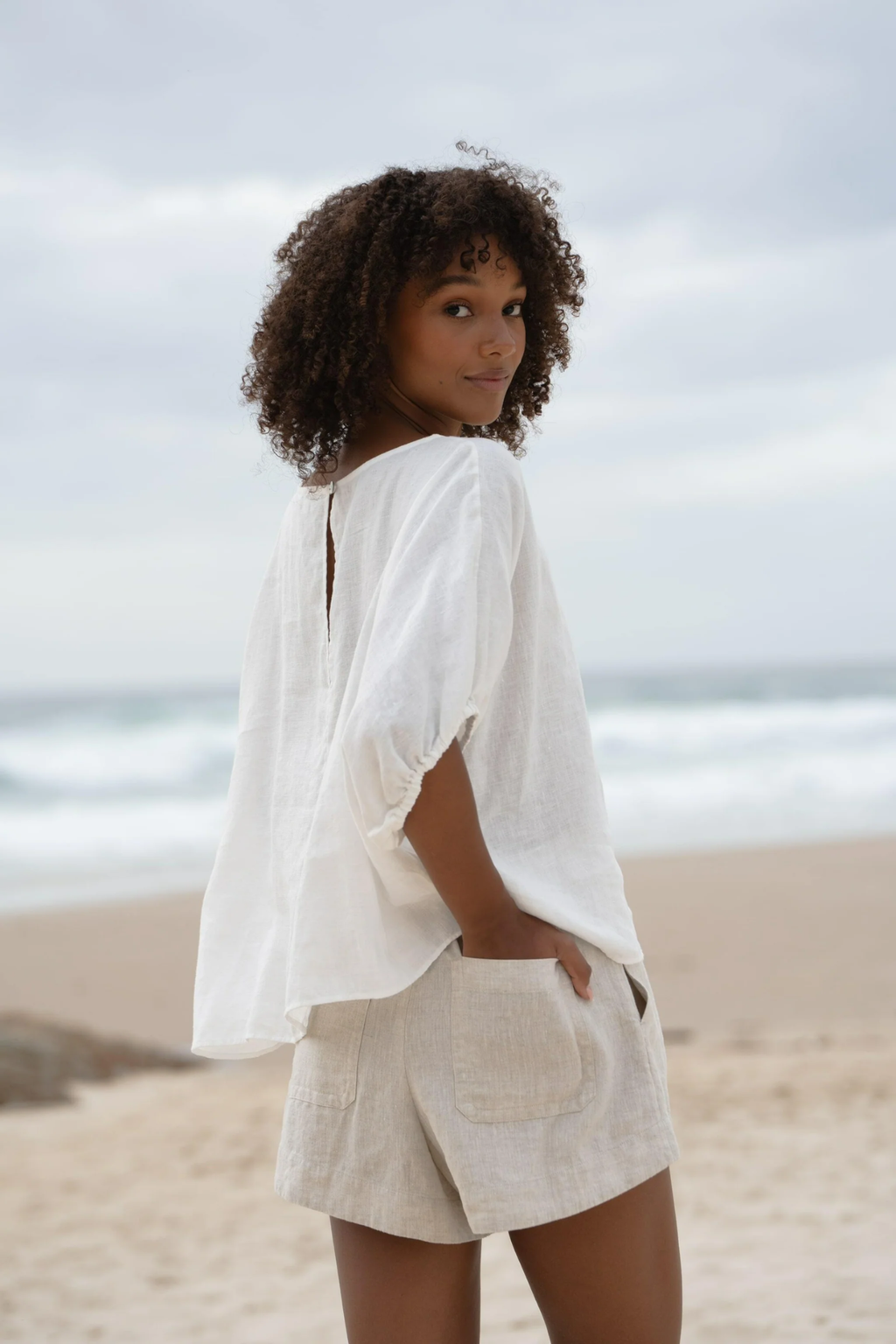 Woman wearing Lilly Pilly LPW23-T001 Tina Linen Top Ivory by Lilly Pilly, shop Lilly Pilly at Dotique on beach background