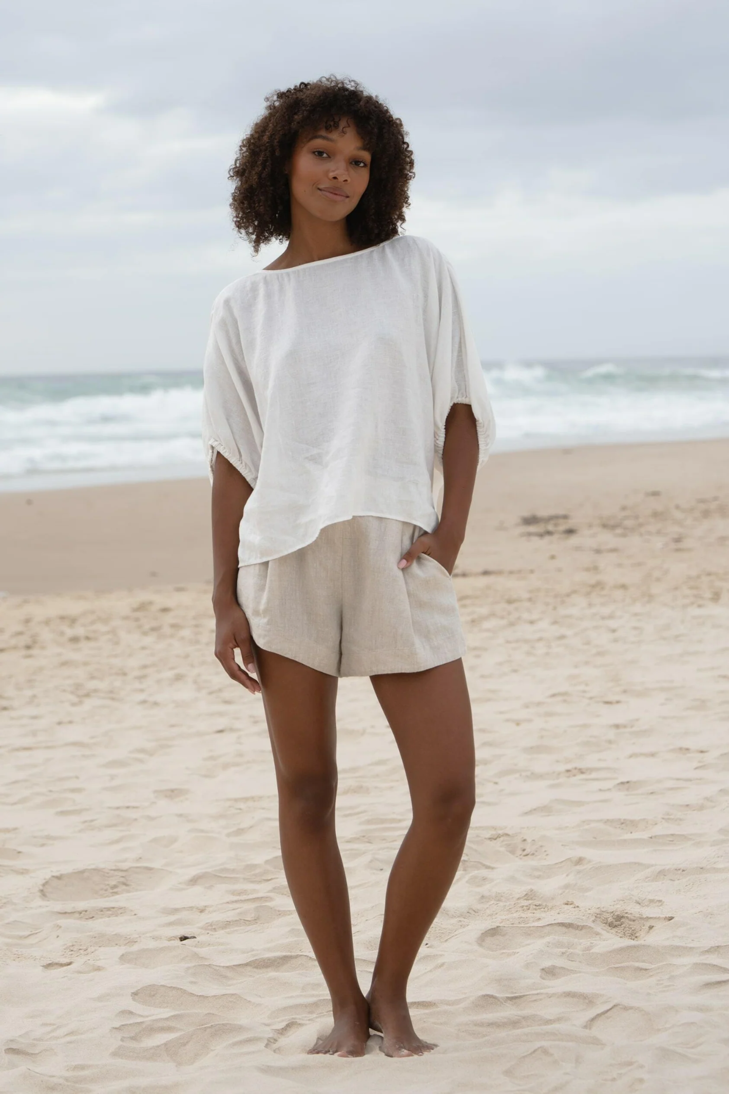 Woman wearing Lilly Pilly LPW23-T001 Tina Linen Top Ivory by Lilly Pilly standing on beach, shop Lilly Pilly at Dotique.