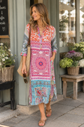 A woman wearing a colorful bohemian midi shirt dress with a pink, blue, and orange pattern, standing on a sidewalk in front of a shop.