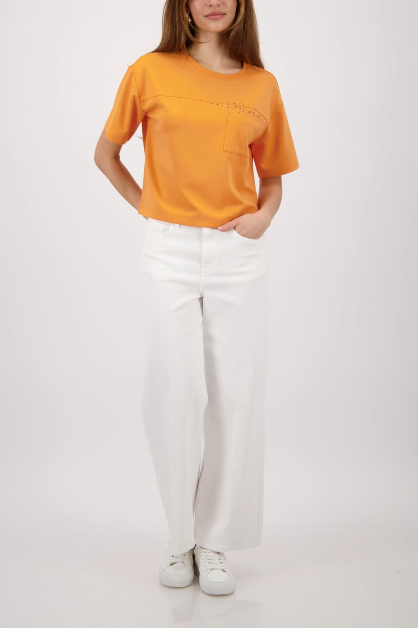 Woman wearing Monari 410127 Sweatshirt with Rhinestones Orange paired with white pants, shop Monari at Dotique.