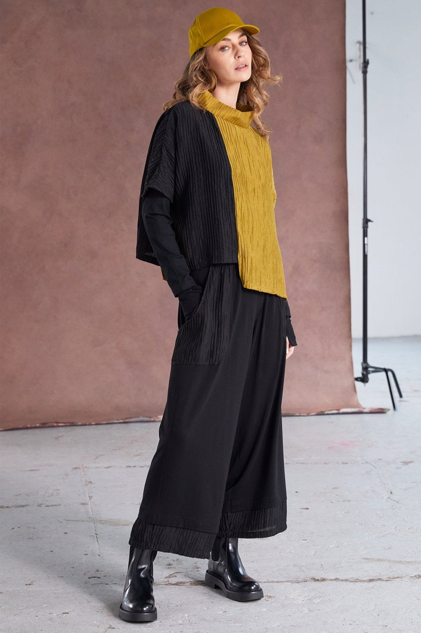 Woman wearing a black outfit with a yellow sweater and hat against a brown backdrop