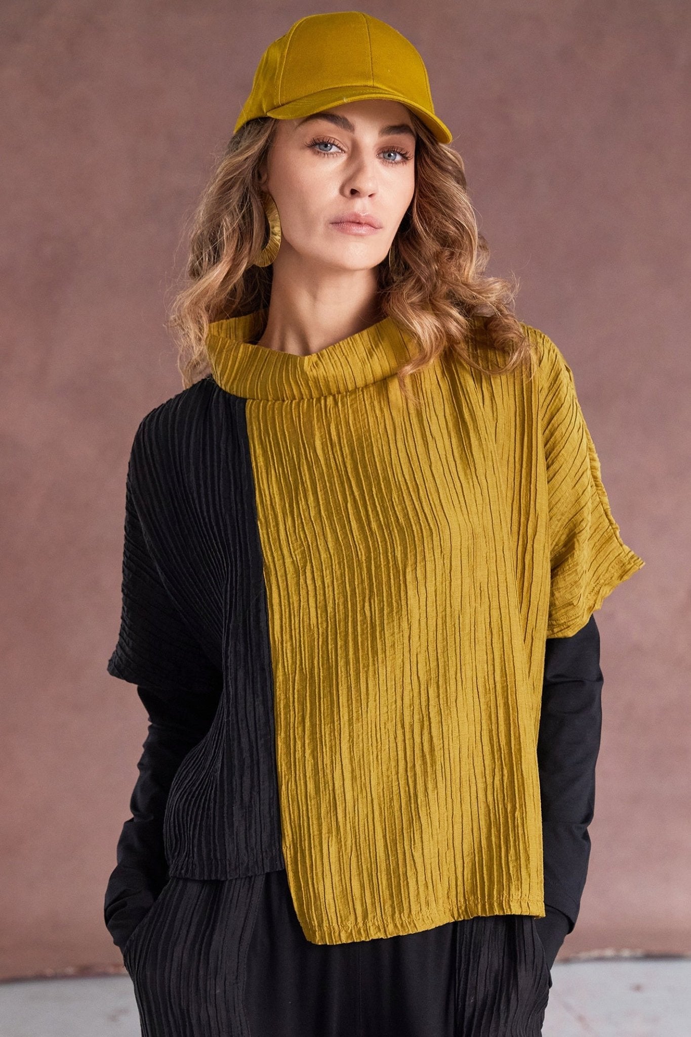 Woman wearing a mustard yellow sweater and cap against a brown background