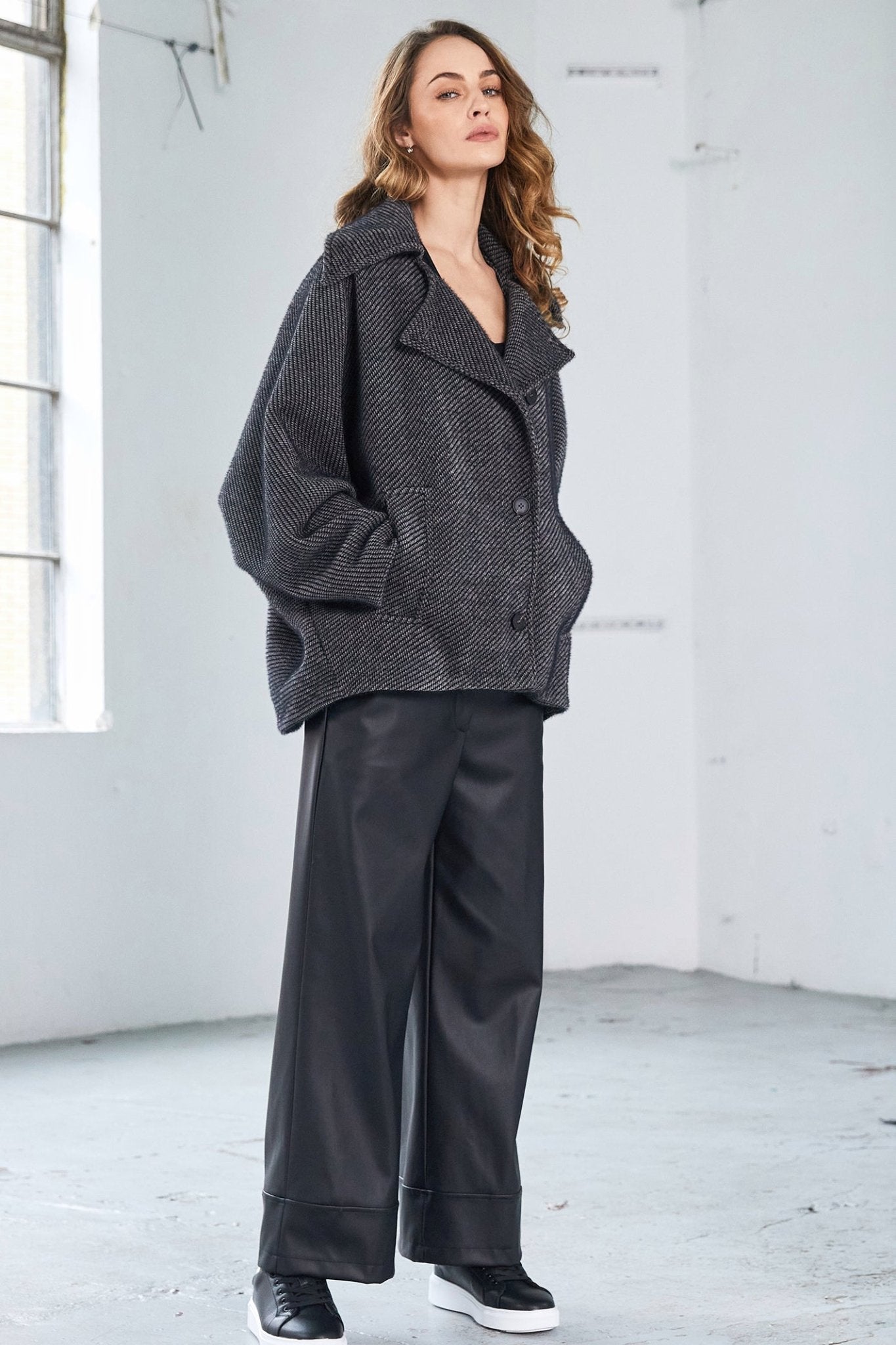 Woman wearing a gray textured coat and black pants in a minimalistic setting