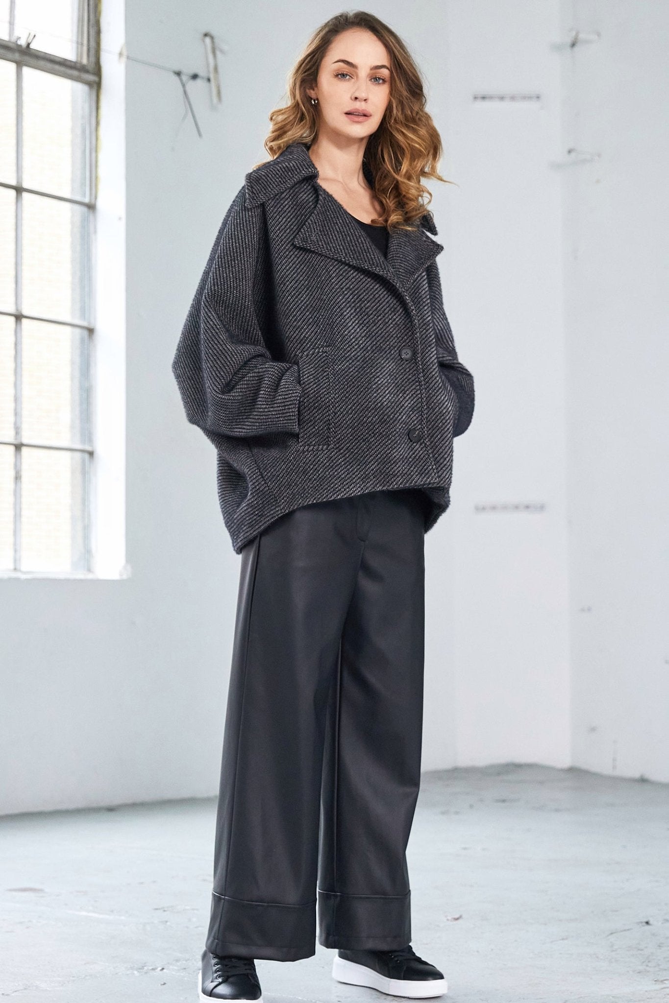 Woman wearing a dark gray coat and pants in a minimalistic room.