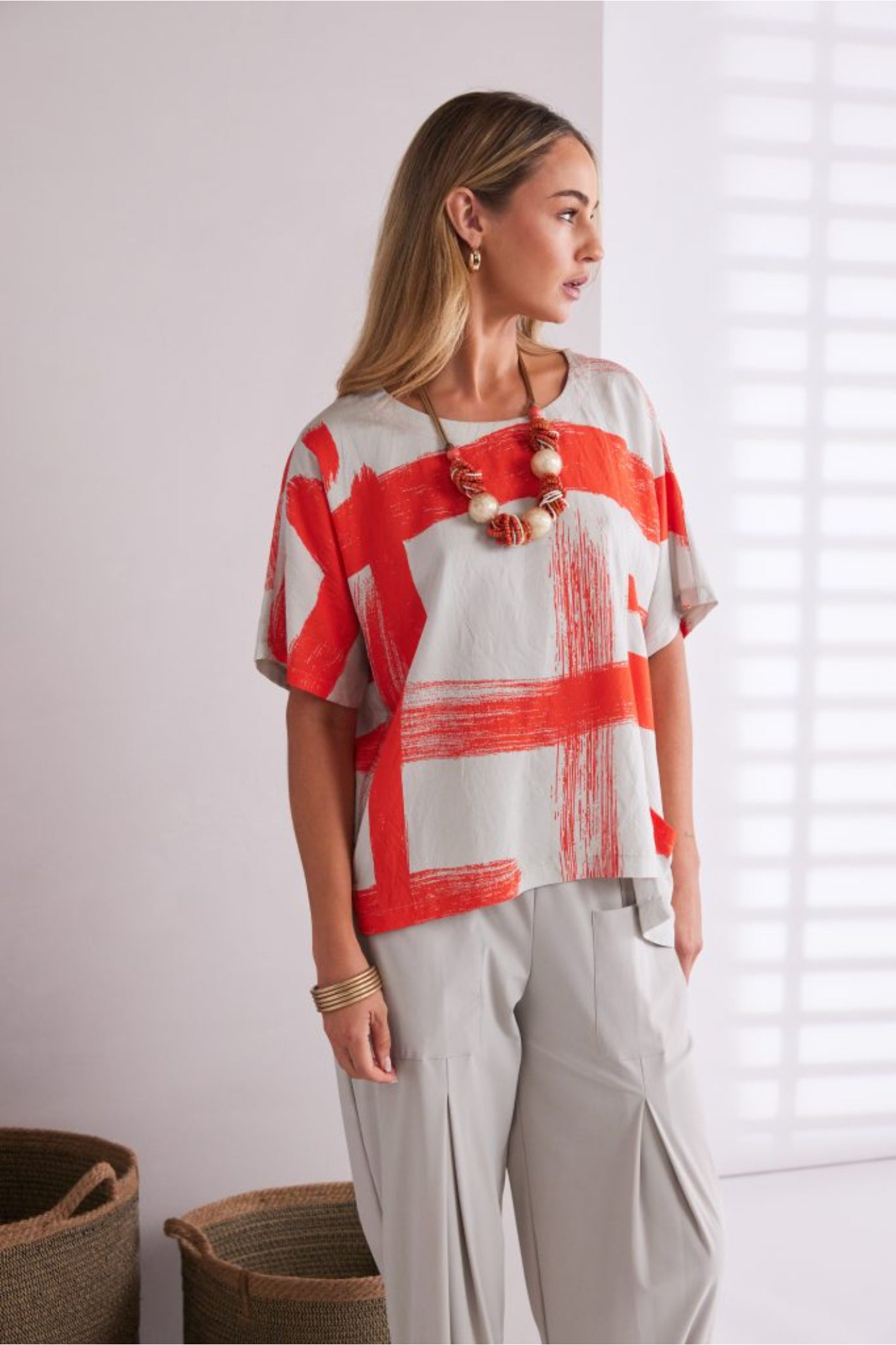 NAYA paintwork print top in coral and ivory featuring an abstract brushstroke design, round neckline, deep cuffed short sleeves and a relaxed fit with a shaped hemline. Shop at Dotique Chesterfield.