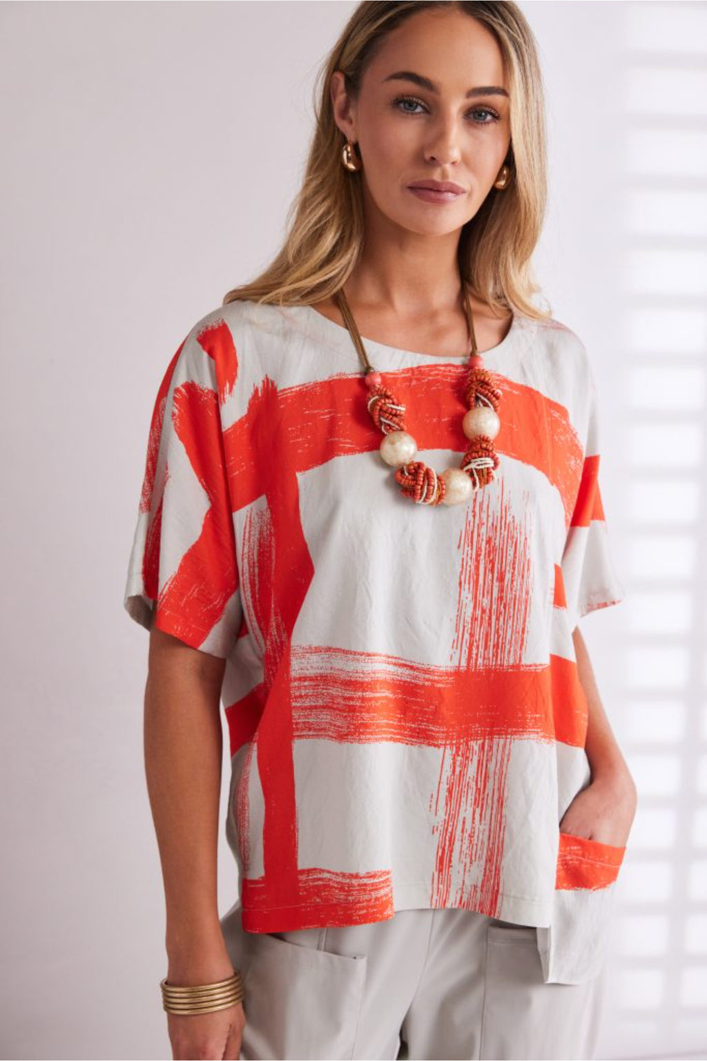 NAYA paintwork print top in coral and ivory featuring an abstract brushstroke design, round neckline, deep cuffed short sleeves and a relaxed fit with a shaped hemline. Shop at Dotique Chesterfield.