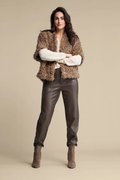 Woman wearing a brown textured jacket, dark leather trousers, and ankle boots against a neutral background