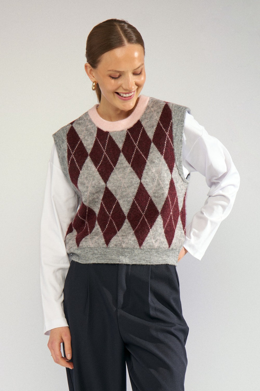 Shop the Nümph NUTIKLA Vest in Medium Grey Melange at Dotique. A wool blend argyle knitted vest in grey and burgundy with a contrasting pink neckline.