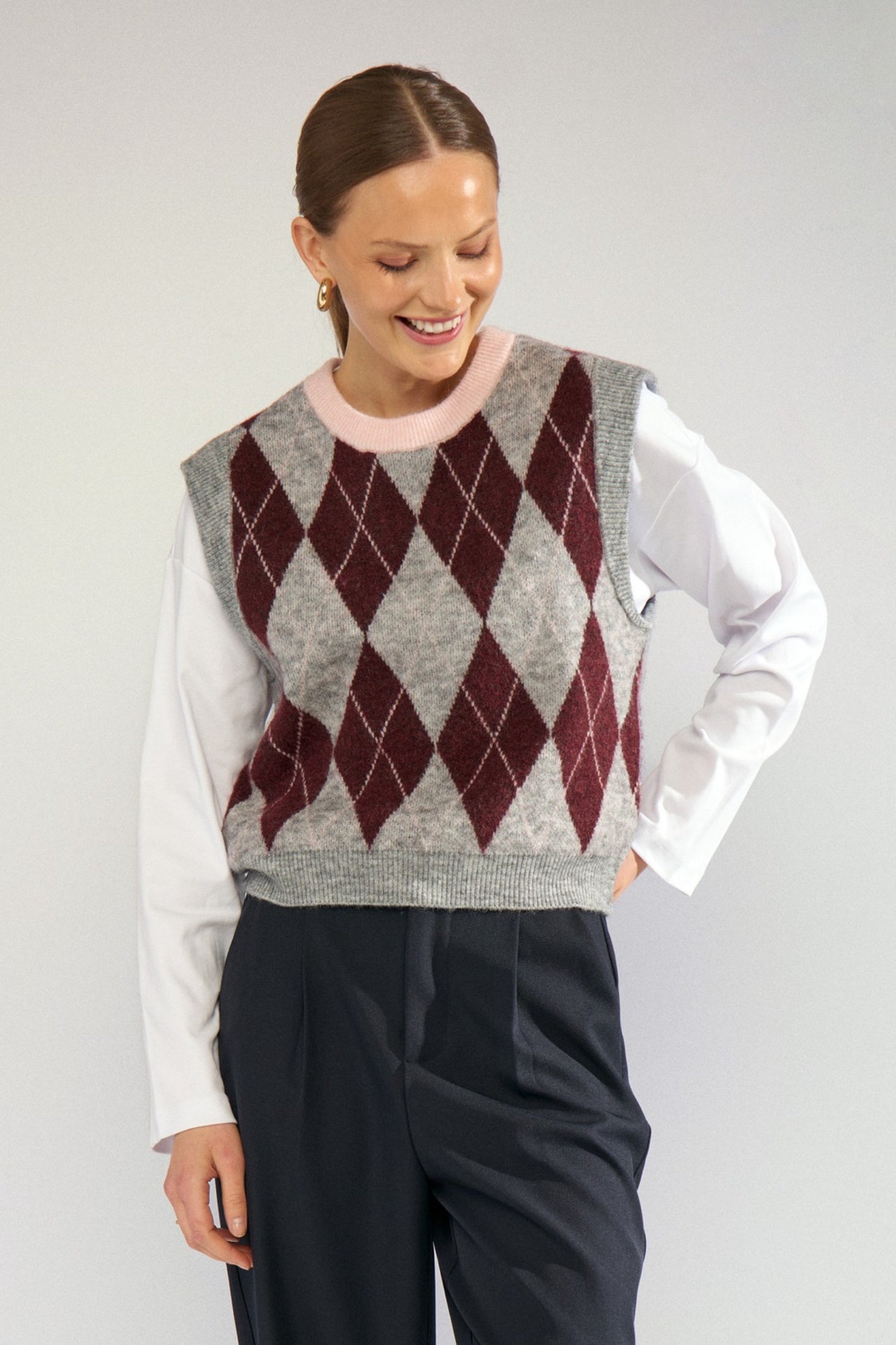 Shop the Nümph NUTIKLA Vest in Medium Grey Melange at Dotique. A wool blend argyle knitted vest in grey and burgundy with a contrasting pink neckline.