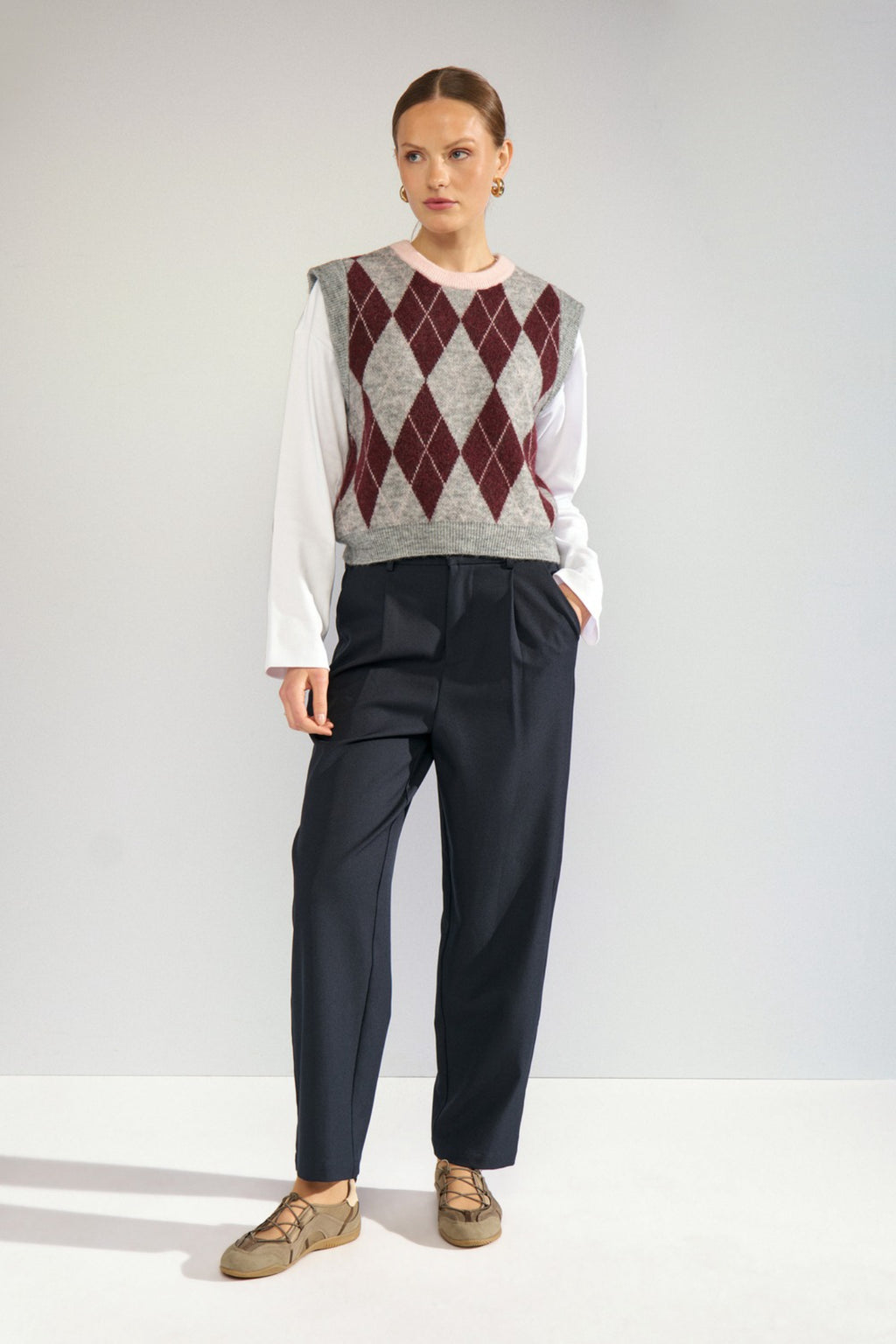 Shop the Nümph NUTIKLA Vest in Medium Grey Melange at Dotique. A wool blend argyle knitted vest in grey and burgundy with a contrasting pink neckline.