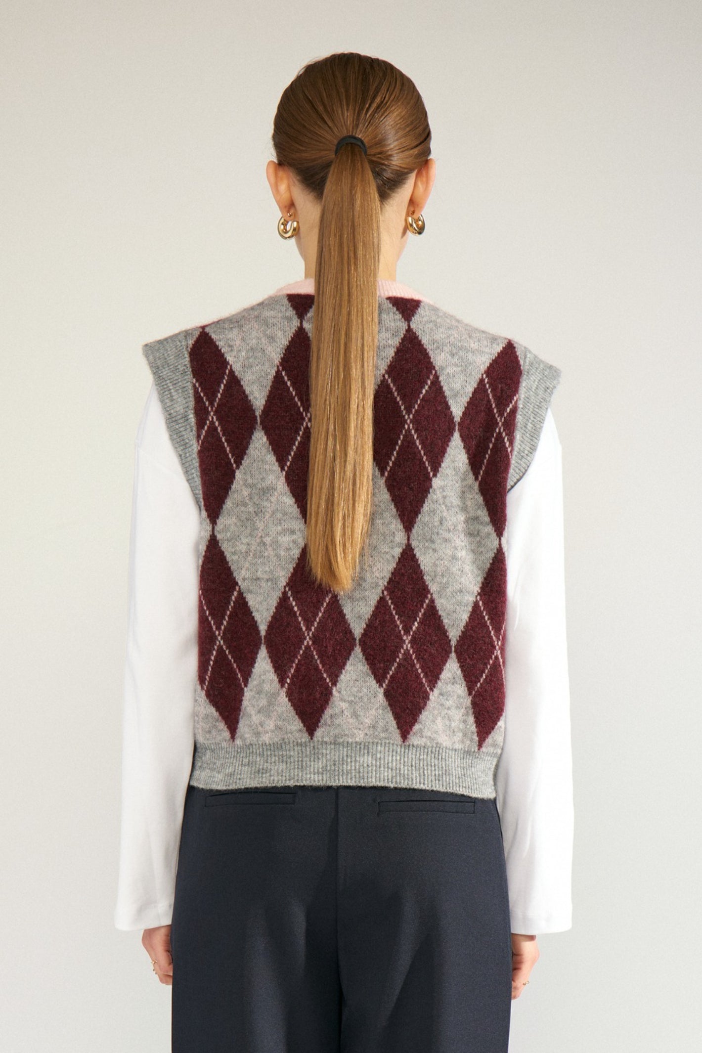 Shop the Nümph NUTIKLA Vest in Medium Grey Melange at Dotique. A wool blend argyle knitted vest in grey and burgundy with a contrasting pink neckline.