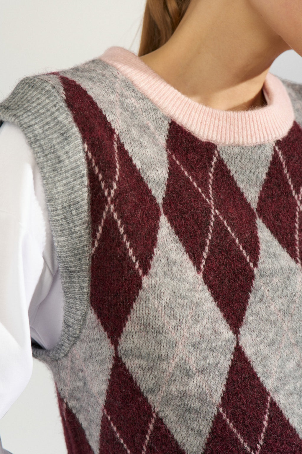 Shop the Nümph NUTIKLA Vest in Medium Grey Melange at Dotique. A wool blend argyle knitted vest in grey and burgundy with a contrasting pink neckline.