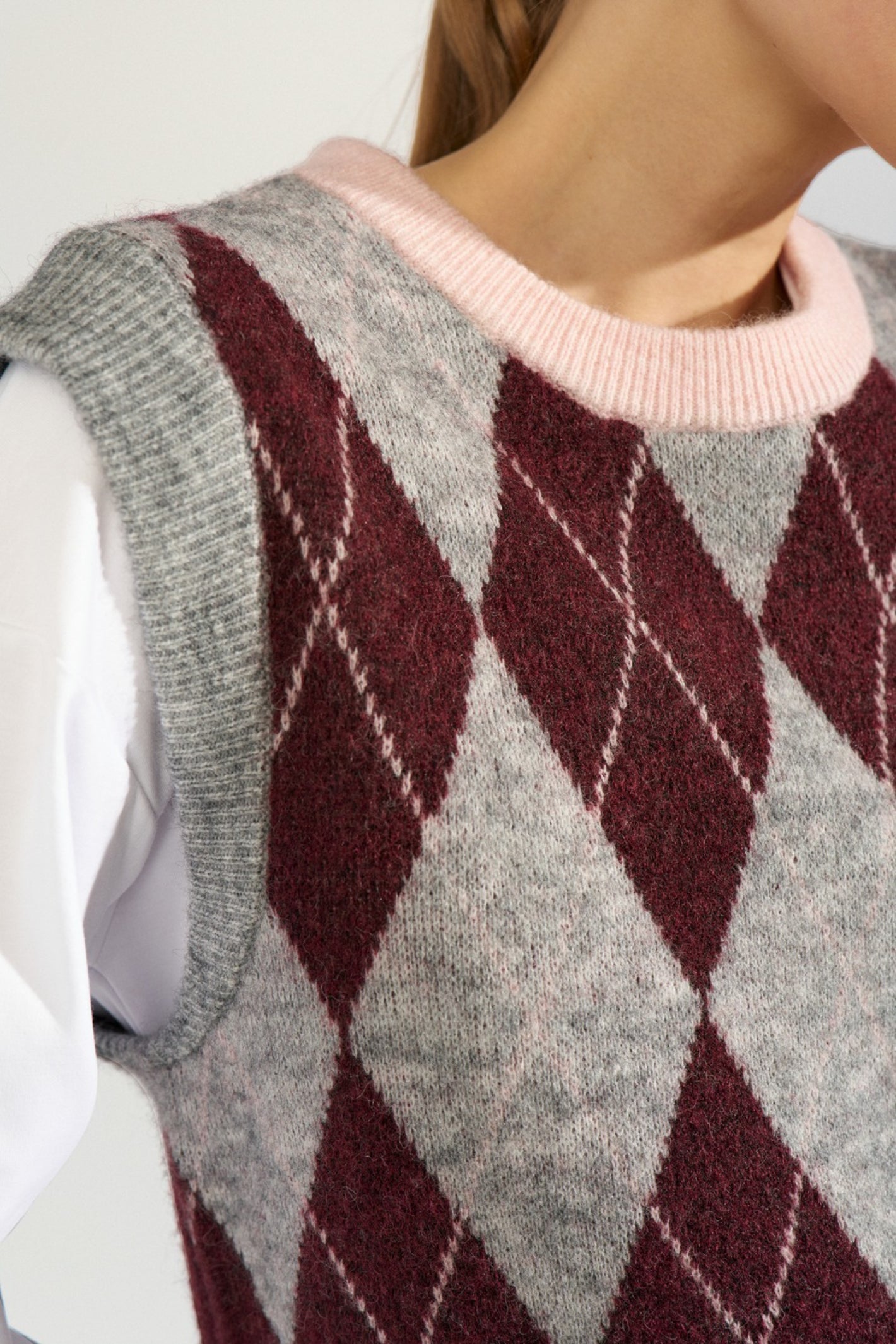 Shop the Nümph NUTIKLA Vest in Medium Grey Melange at Dotique. A wool blend argyle knitted vest in grey and burgundy with a contrasting pink neckline.