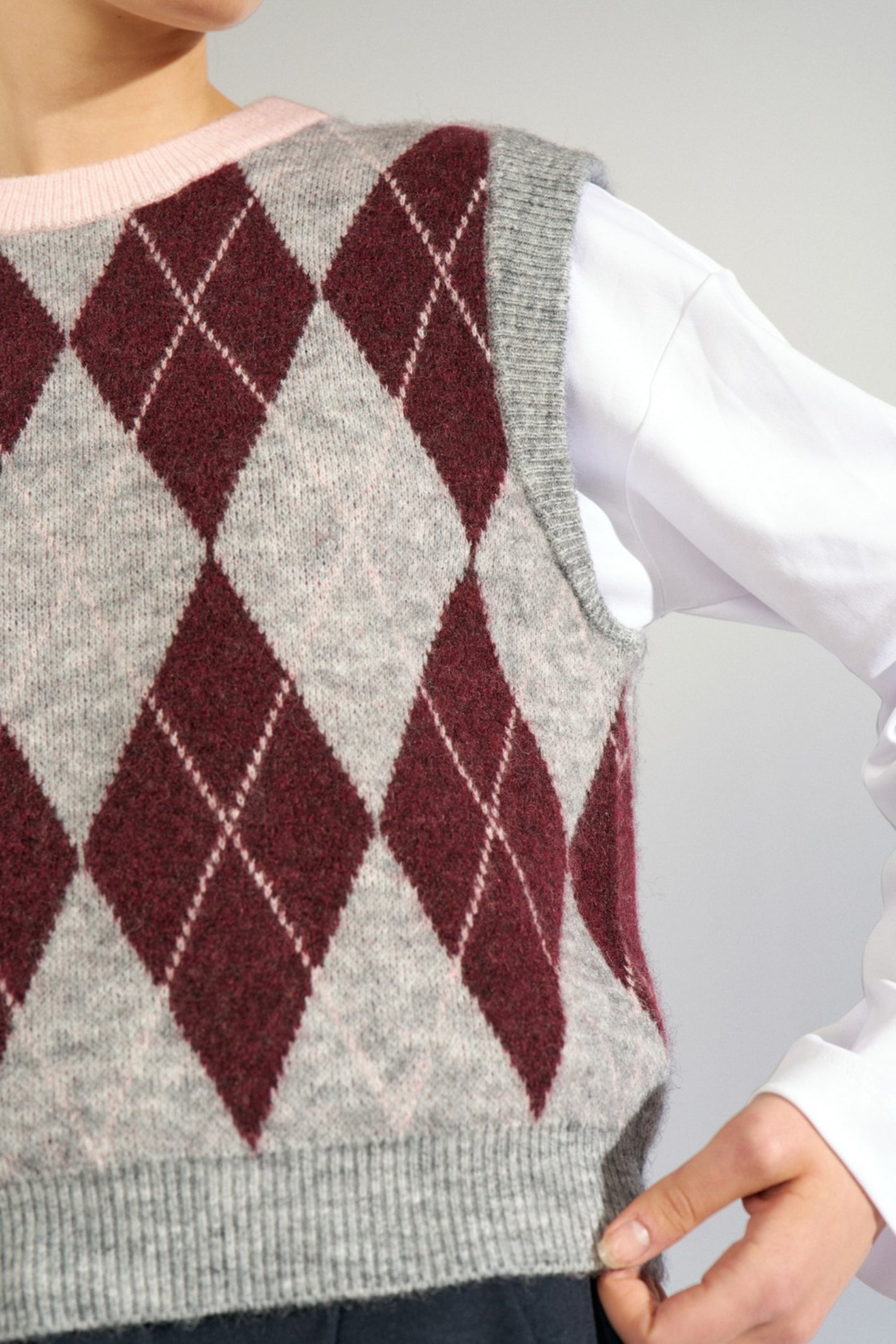 Shop the Nümph NUTIKLA Vest in Medium Grey Melange at Dotique. A wool blend argyle knitted vest in grey and burgundy with a contrasting pink neckline.
