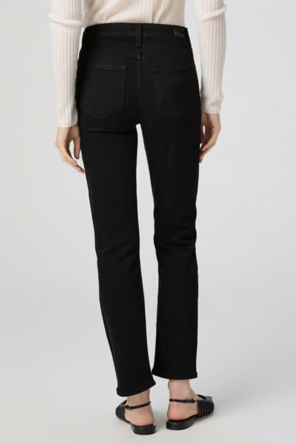 Rear view of a woman wearing PAIGE Cindy High Rise Straight Ankle Jeans Black Shadow in black paired with flat sandals by PAIGE. Shop PAIGE at Dotique.