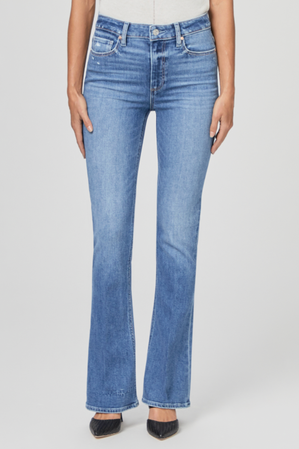 Front view of a model wearing PAIGE Laurel Canyon High Rise Bootcut Jeans Rock Show Distressed in blue denim paired with black pointed shoes by PAIGE. Shop PAIGE at Dotique.