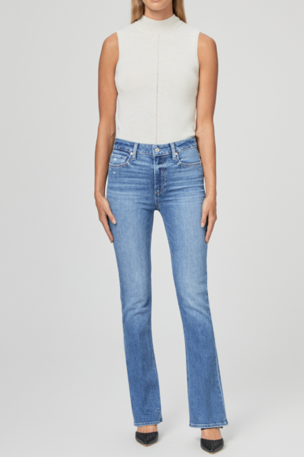 Front view of a model wearing PAIGE Laurel Canyon High Rise Bootcut Jeans Rock Show Distressed in light blue denim paired with a sleeveless beige top. Shop PAIGE at Dotique.