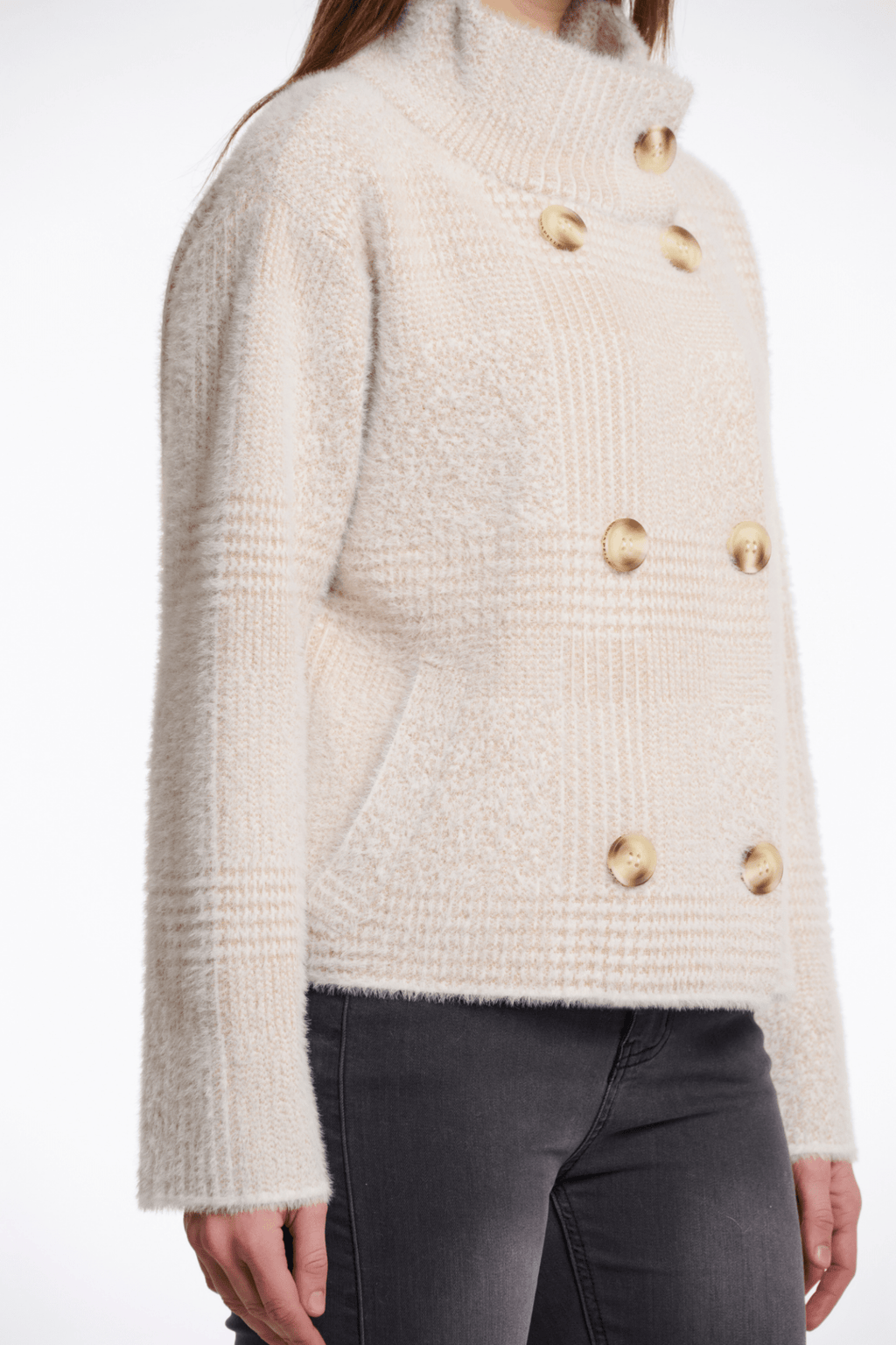 Beige knitted sweater with gold buttons worn by a person on a white background