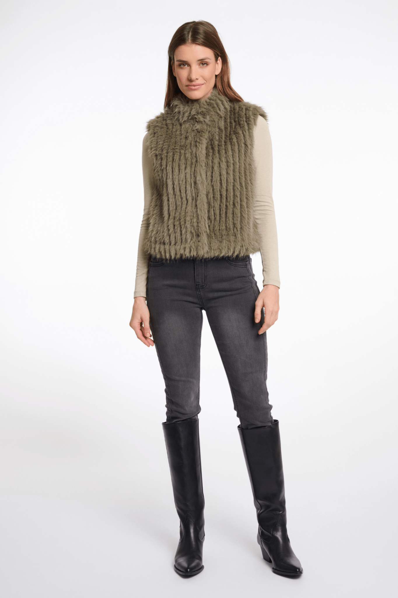 Woman wearing a green knitted vest, gray pants, and black boots on a white background