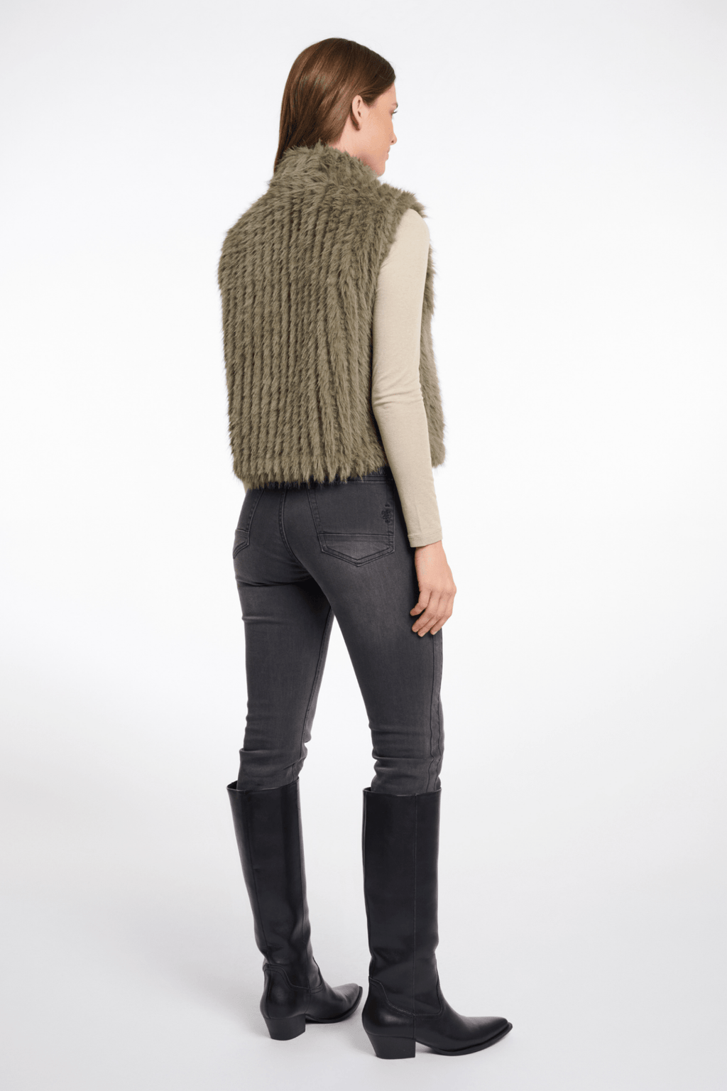 Person wearing a green knitted vest, gray pants, and black boots on a white background