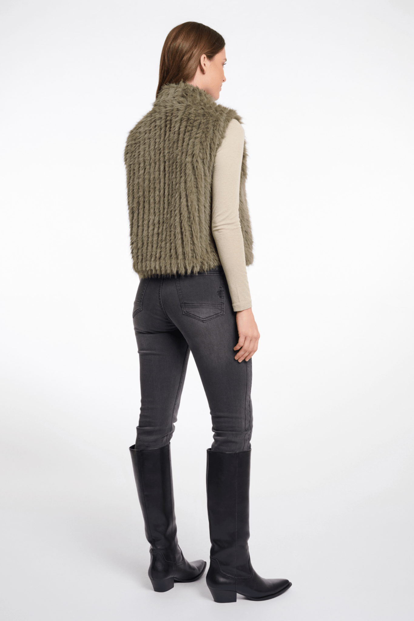 Person wearing a green knitted vest, gray pants, and black boots on a white background