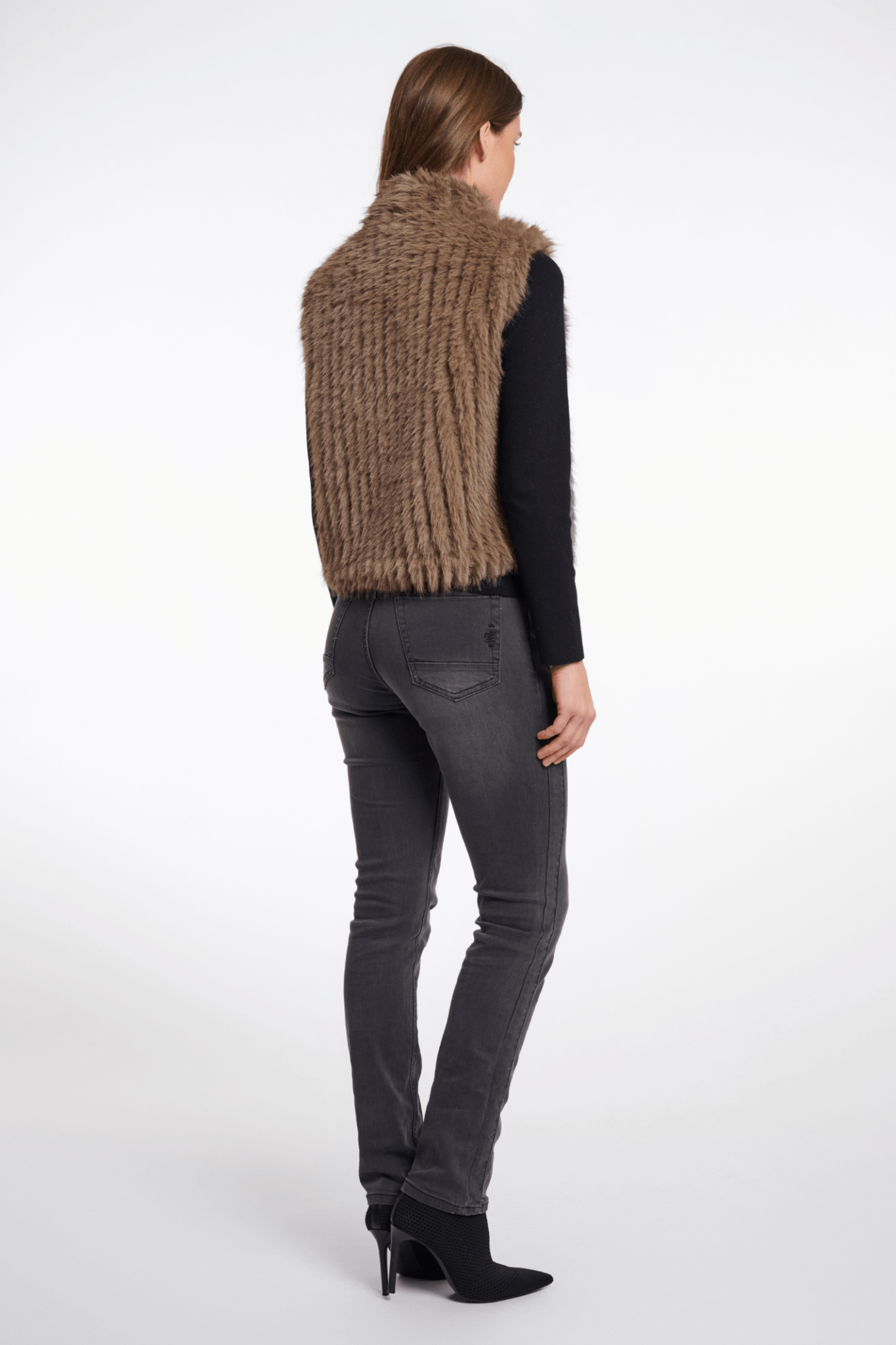 Person wearing a brown knitted vest and gray jeans on a white background