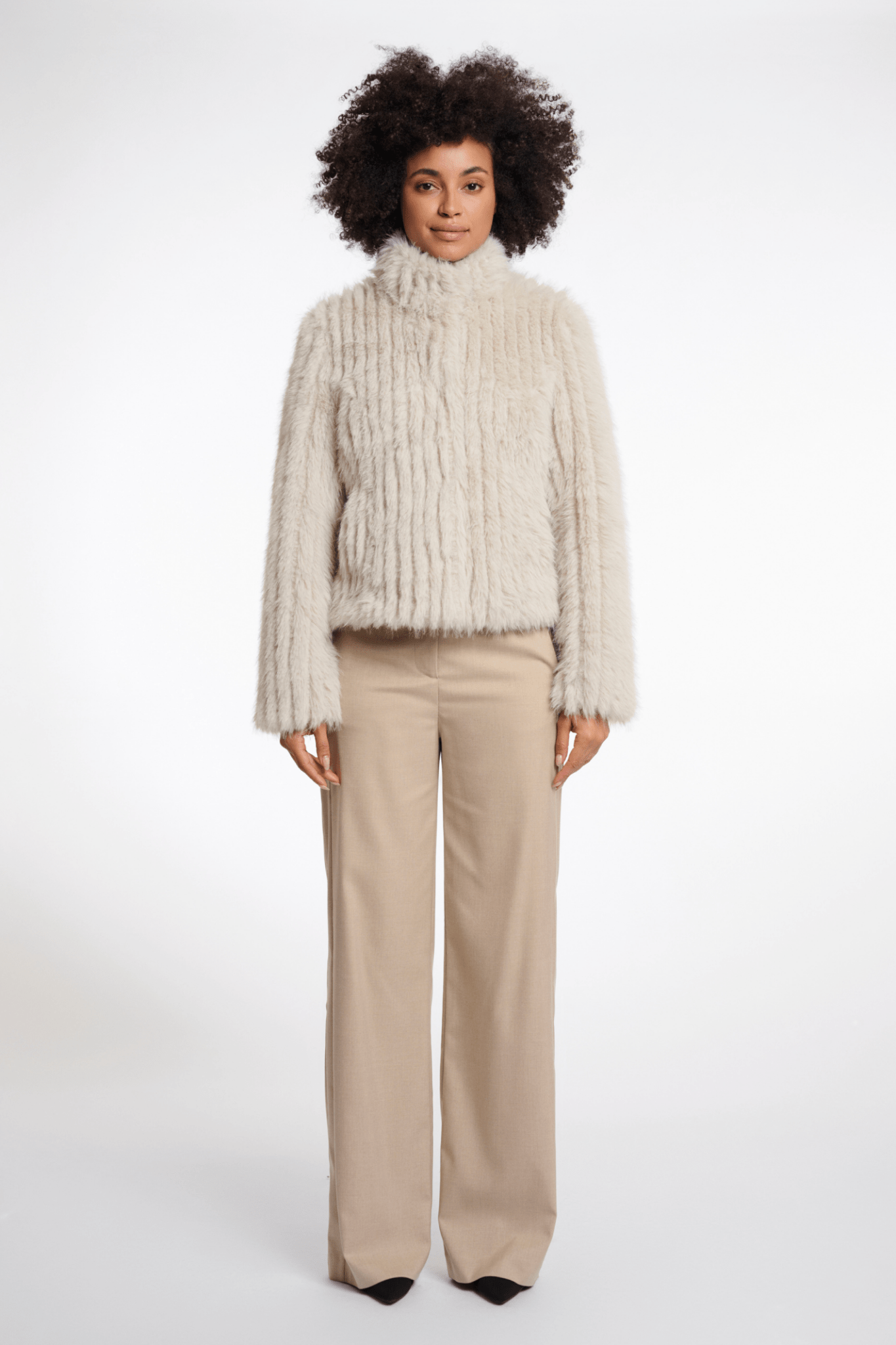 Woman wearing a beige ribbed sweater and beige pants on a white background