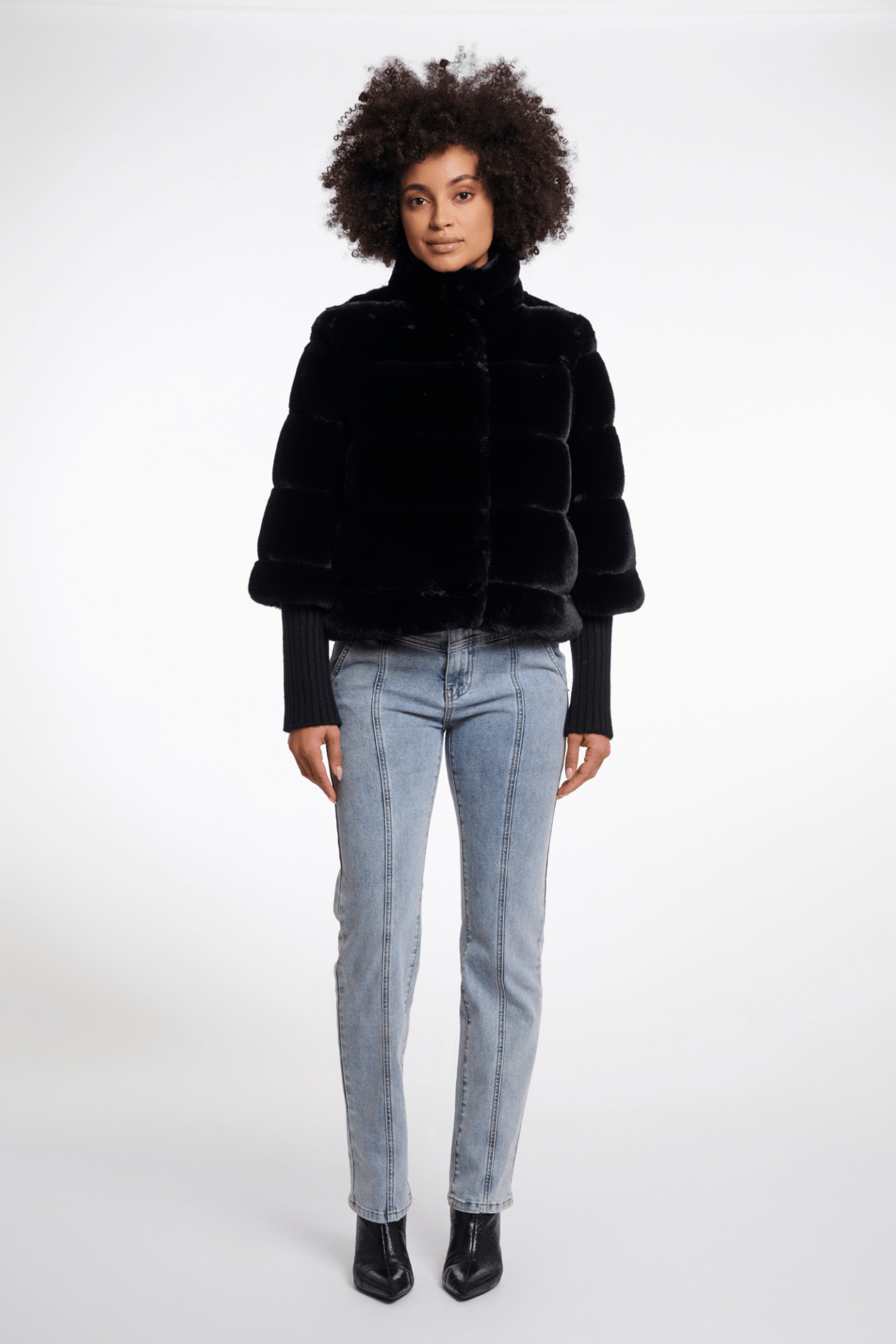 Person wearing a black faux fur jacket and light blue jeans on a white background