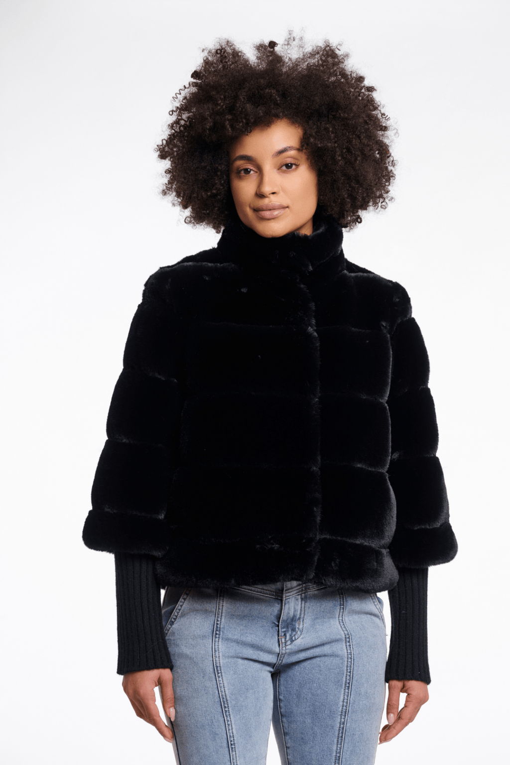 Person wearing a black fur jacket and light blue jeans on a white background