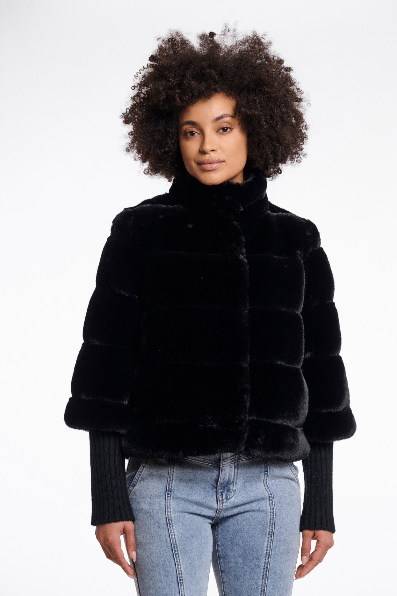 Person wearing a black fur jacket and light blue jeans on a white background