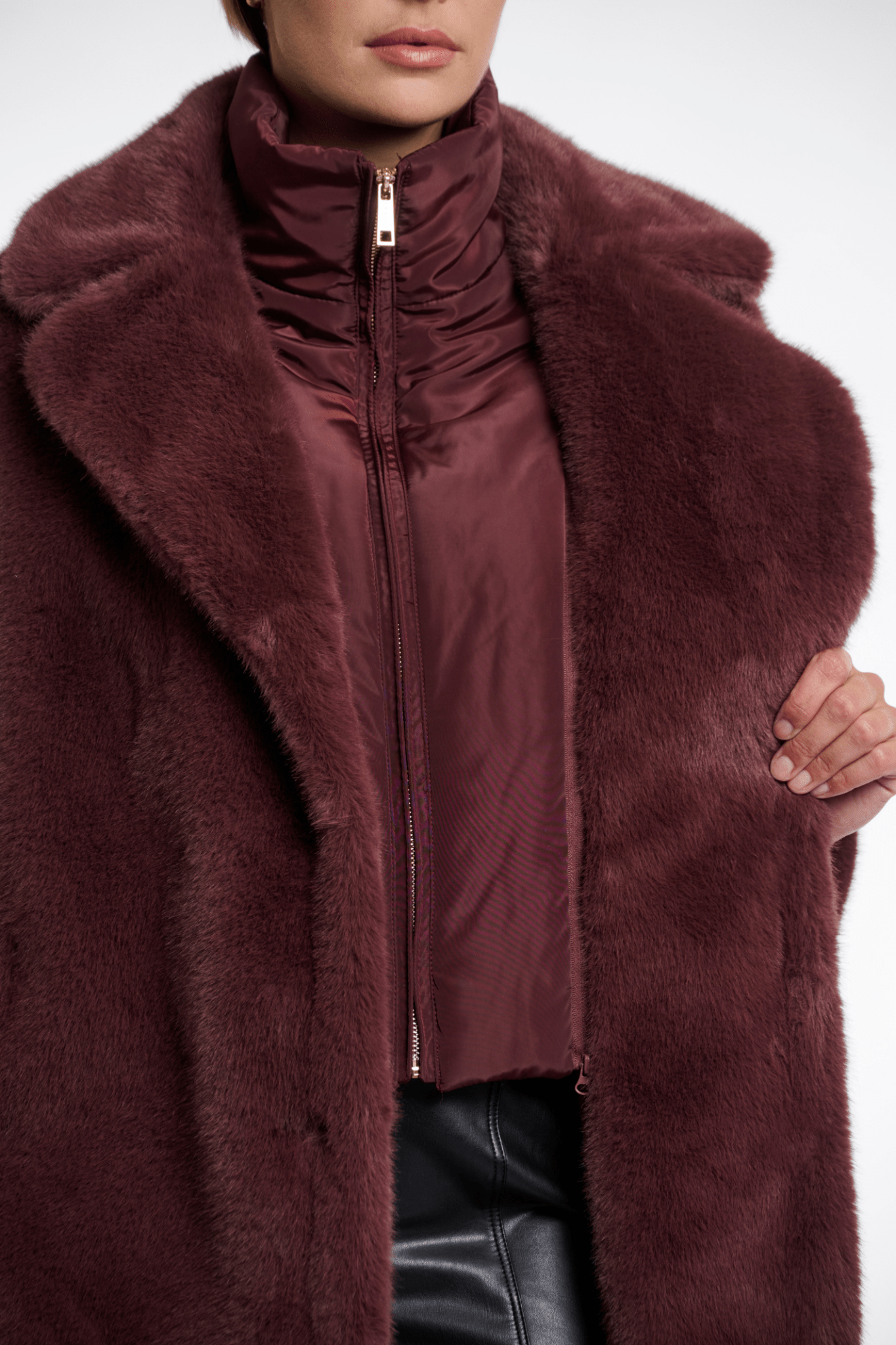 Close-up of a person wearing a burgundy fur coat with a white background